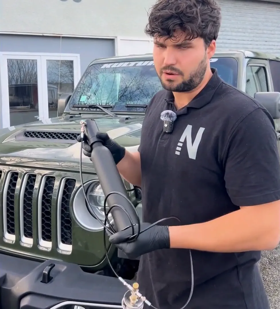 Killian from Nimbus holding the ∆P cartridge, head and hose beside a Jeep at the Nimbus workshop